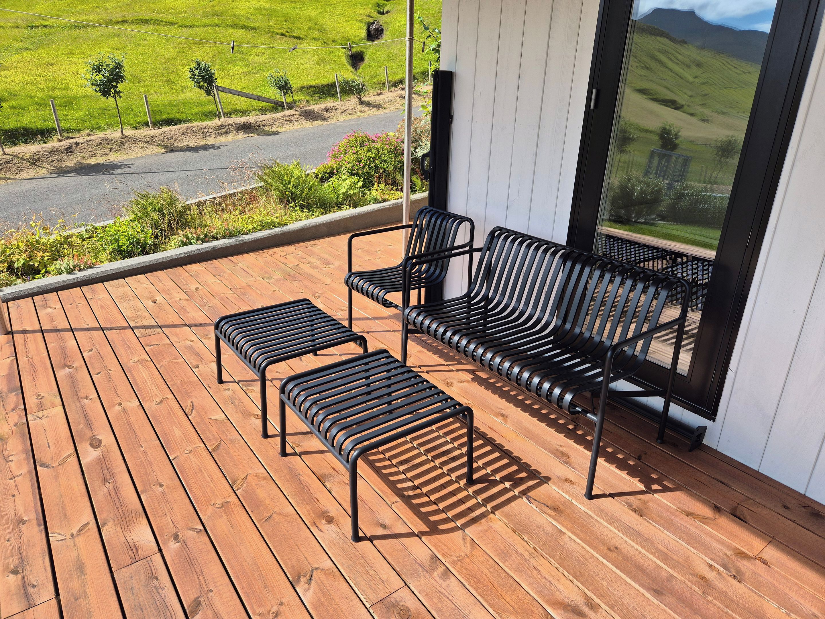 A wooden deck with a sofa and two ottomans, overlooking a green landscape.