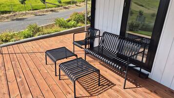 A wooden deck with a sofa and two ottomans, overlooking a green landscape.