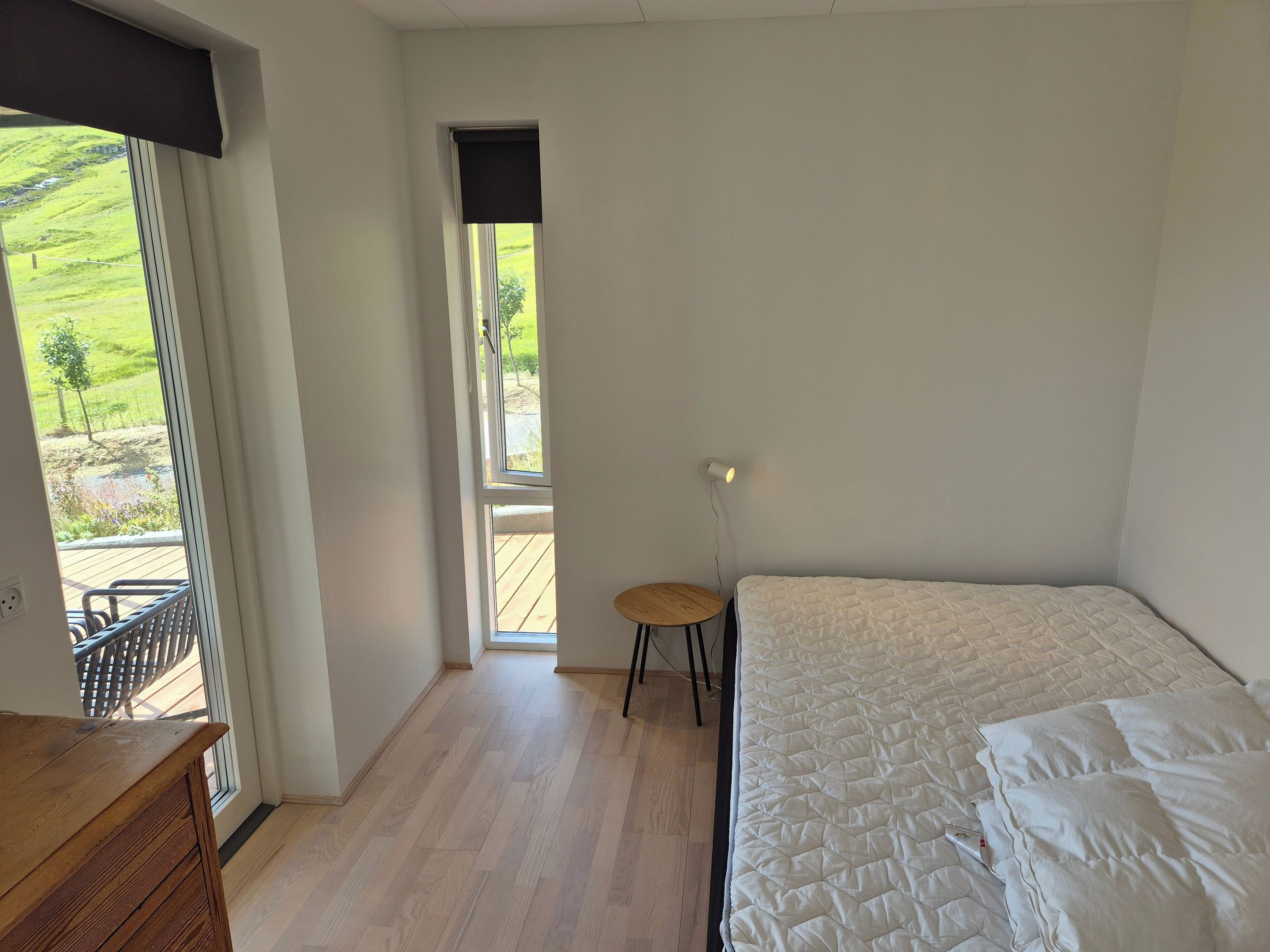 A bedroom with a bed, a small round table, and a view of a green landscape through a window.