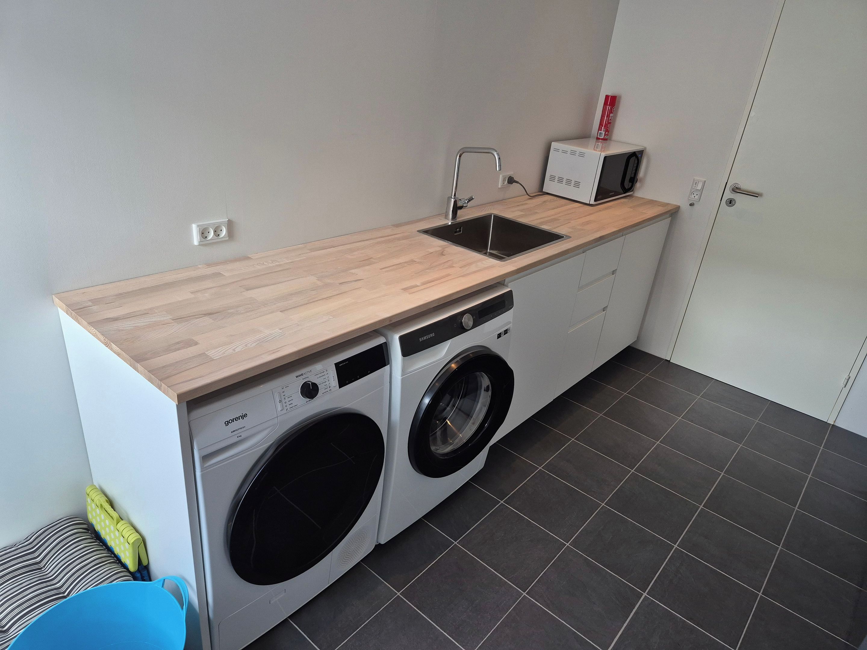 A compact laundry area with a washing machine, dryer, and microwave on a wooden countertop.