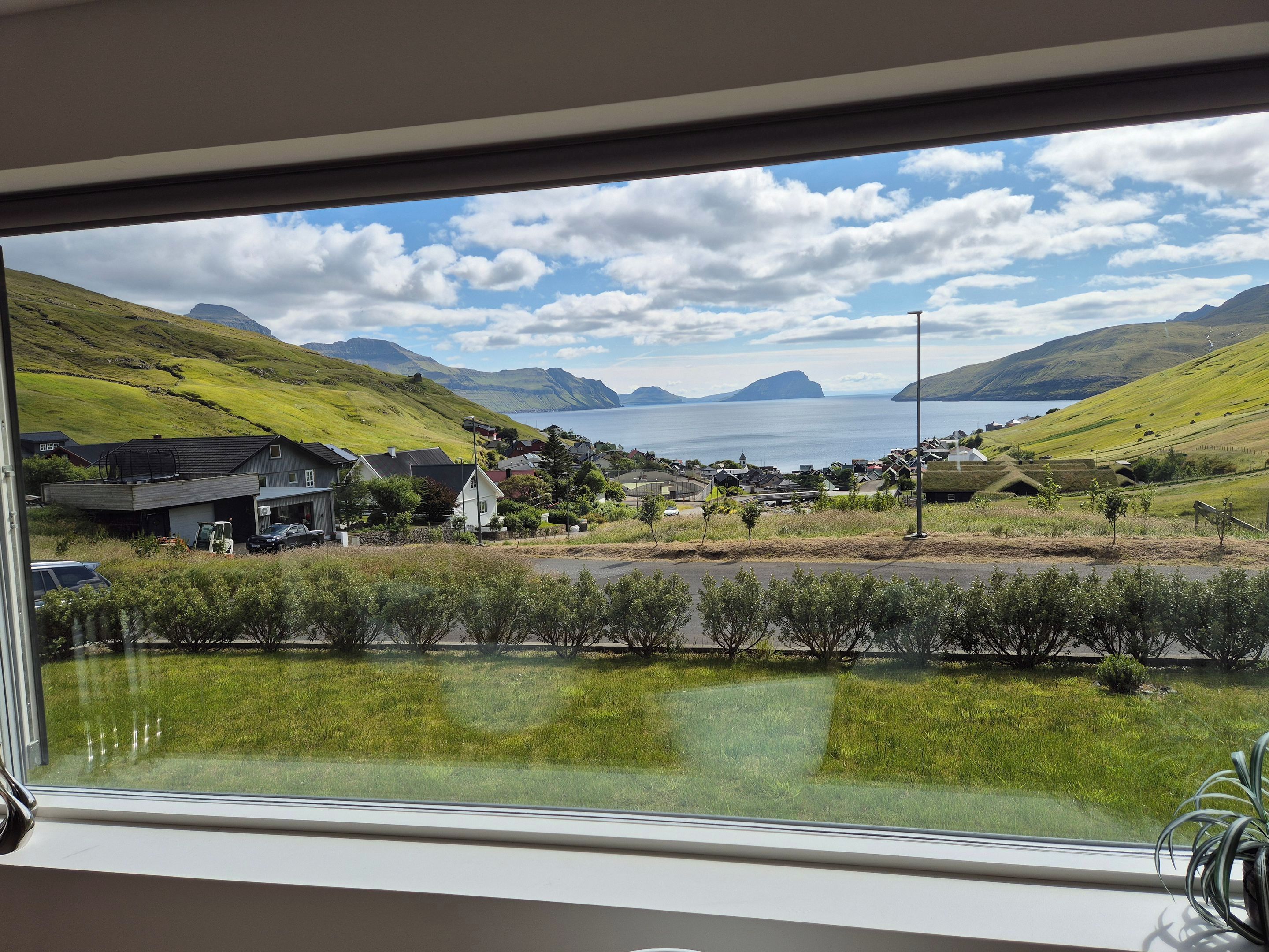 A view from a window overlooking a coastal landscape with houses, a road, and a body of water.