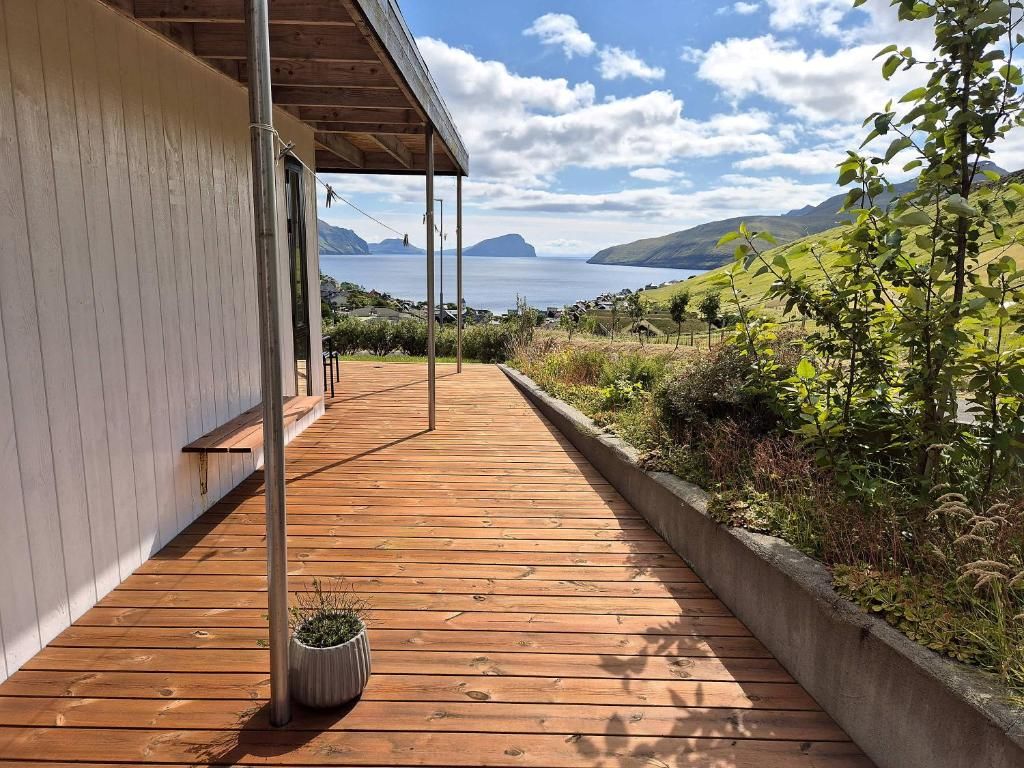 A wooden deck leading to a covered area with a view of the sea and hills.