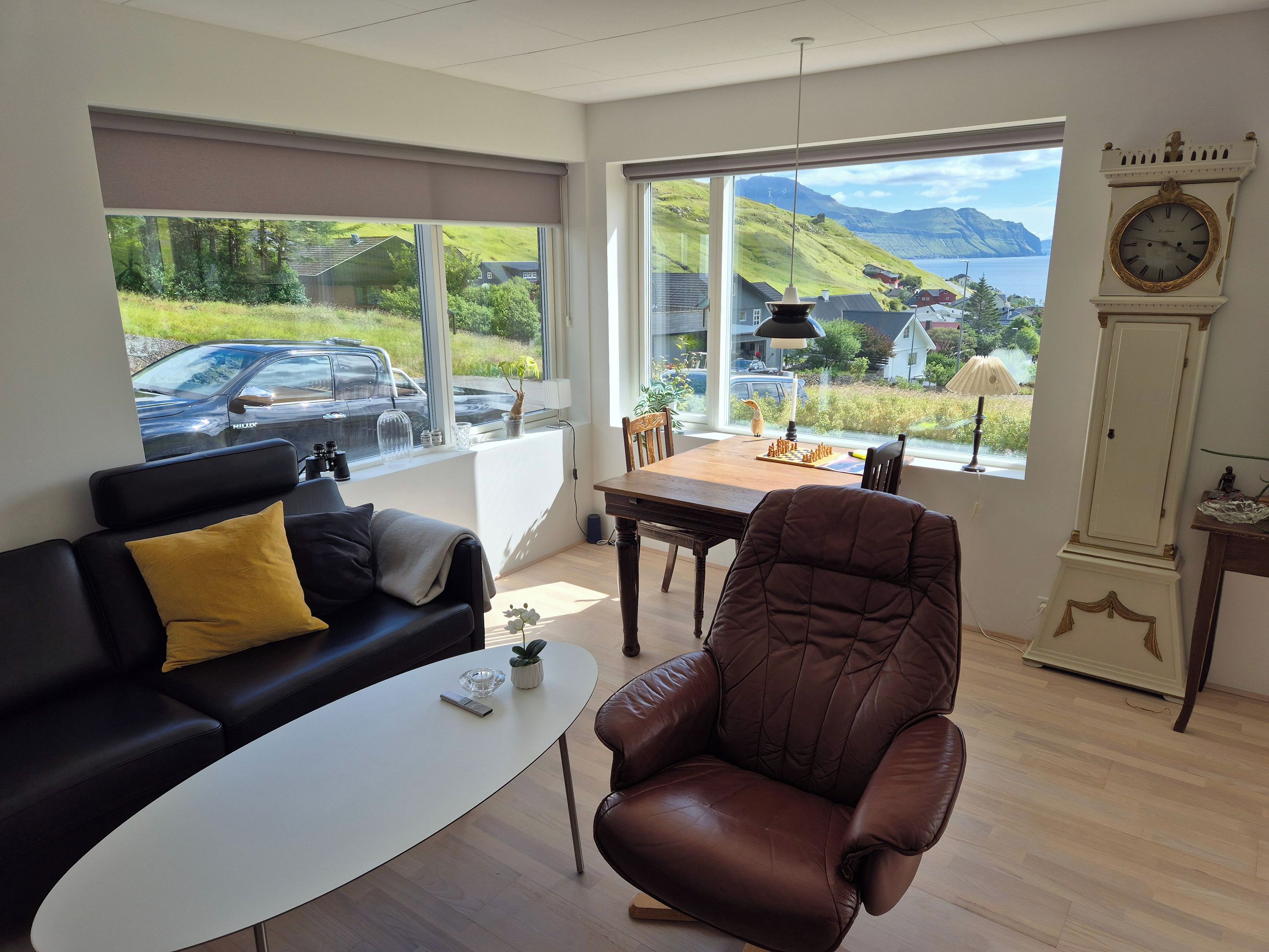 A modern living room with a sofa, armchair, coffee table, and a view of a car parked outside.