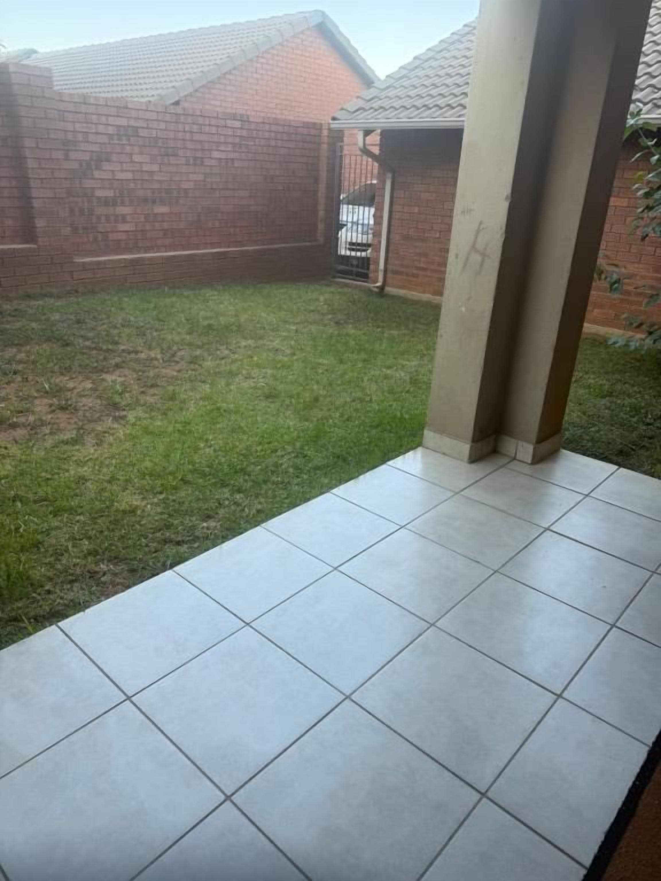 A courtyard with a tiled patio area, a brick wall, and a metal gate.
