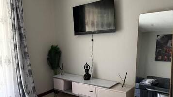Un salon moderne avec un téléviseur à écran plat fixé au mur, une console avec des tiroirs, un grand miroir et un tapis à motifs sur le sol.