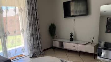 Un salon avec une table basse ronde, un téléviseur à écran plat fixé au mur, un canapé et un tapis à motifs.