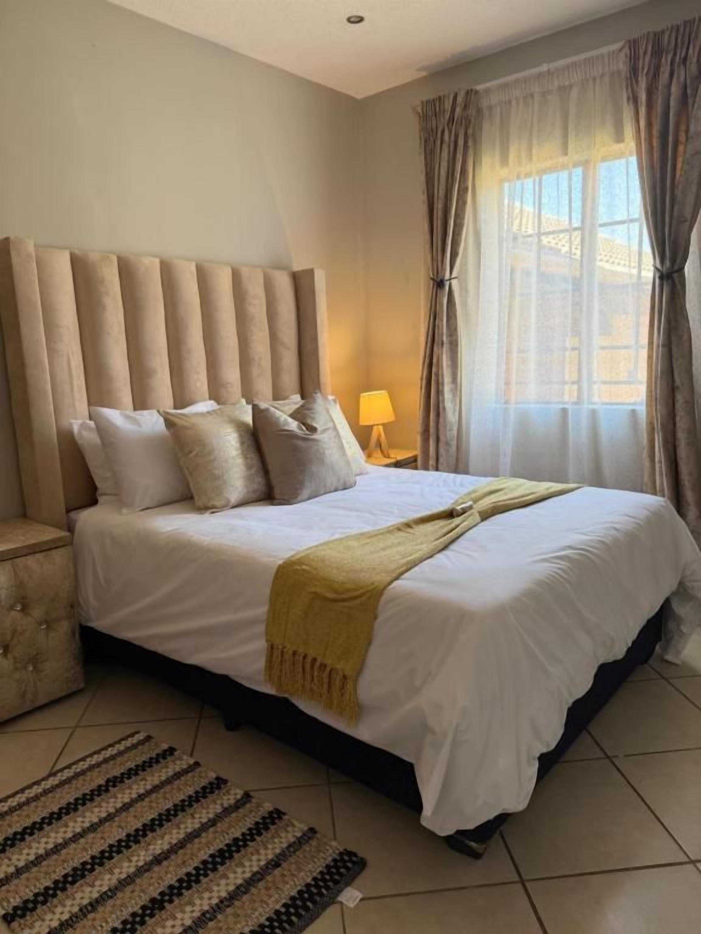 Une chambre d’hôtel avec un grand lit, une table de chevet, une lampe et une fenêtre avec des rideaux.