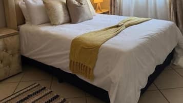 Une chambre d’hôtel avec un grand lit, une table de chevet, une lampe et une fenêtre avec des rideaux.