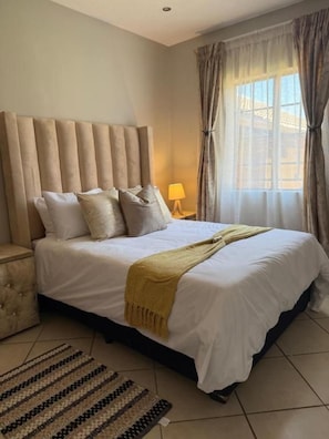 Une chambre d’hôtel avec un grand lit, une table de chevet, une lampe et une fenêtre avec des rideaux.