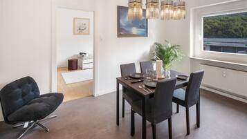 Un comedor con una mesa lista para cuatro, una silla moderna, una planta en maceta y vistas al exterior a través de un ventanal.