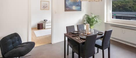 A dining area with a table set for four, a modern chair, a potted plant, and a view of the outdoors through a window.