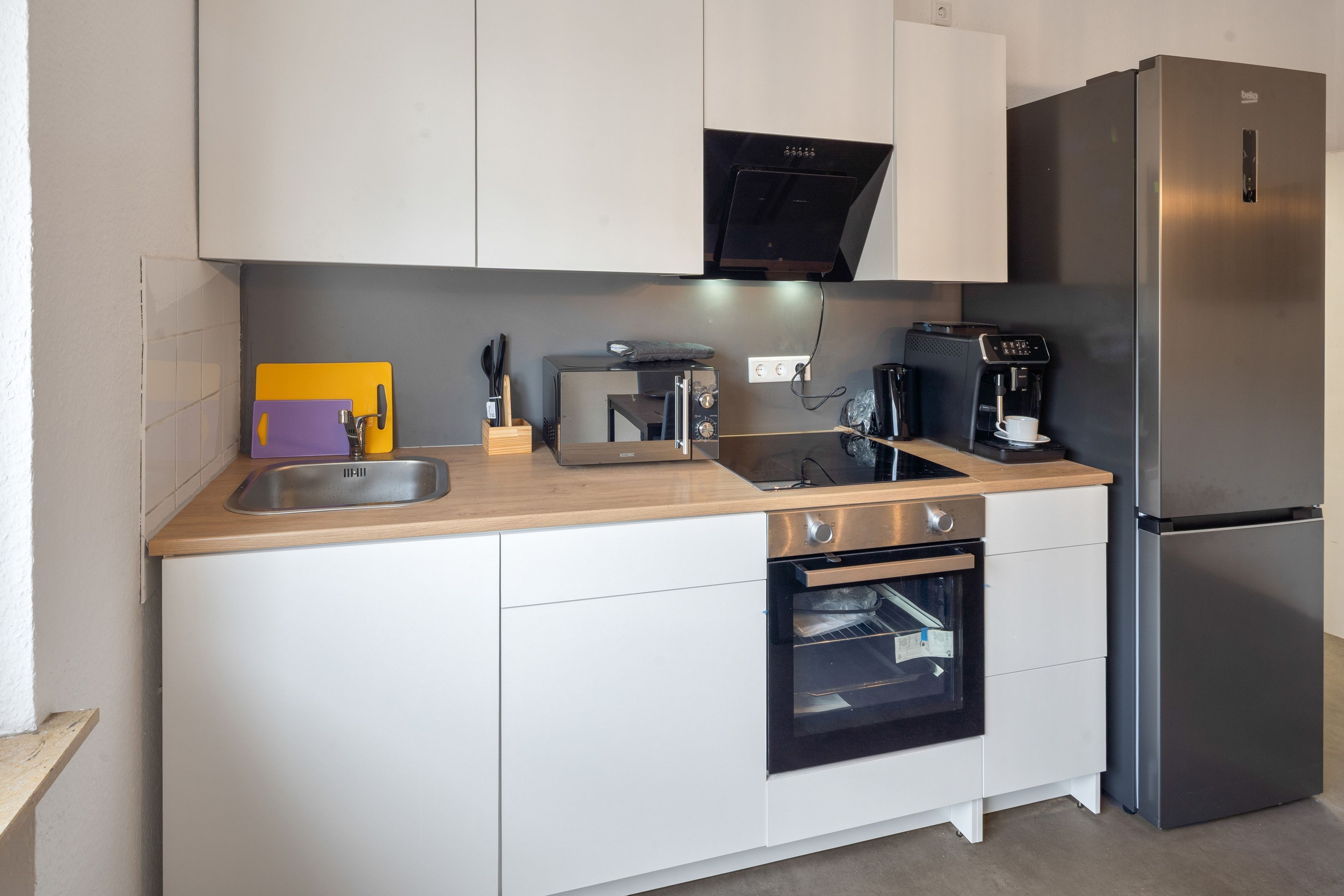 Una cocina compacta con un refrigerador de acero inoxidable, horno empotrado, cafetera y microondas.
