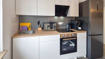 Una cocina compacta con un refrigerador de acero inoxidable, horno empotrado, cafetera y microondas.