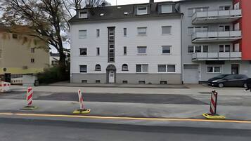 Ein mehrstöckiges Gebäude mit einem zentralen Eingang, Balkonen und einem Parkplatz mit Barrieren.