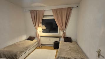Una habitación pequeña y bien iluminada con dos camas individuales, un escritorio y un radiador.