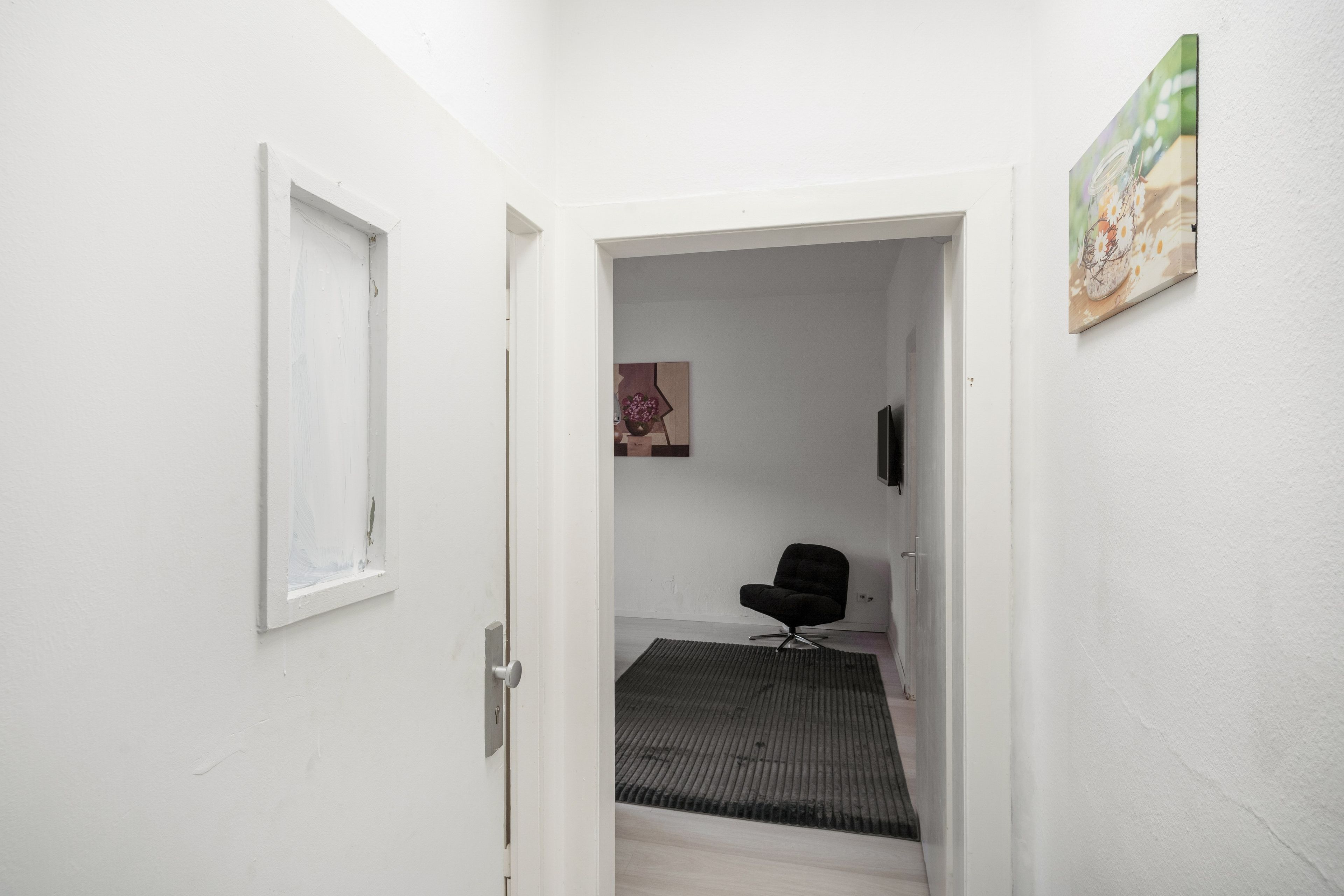 A narrow hallway with a door leading to a room with a black chair and a rug.