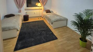 Ein kleiner, gut beleuchteter Raum mit zwei Betten, einem Heizkörper, einer Lampe und einer Topfpflanze.