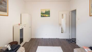Una habitación con una puerta blanca, un armario blanco, una mesita con un vaso, una alfombra blanca y un cuadro en la pared.