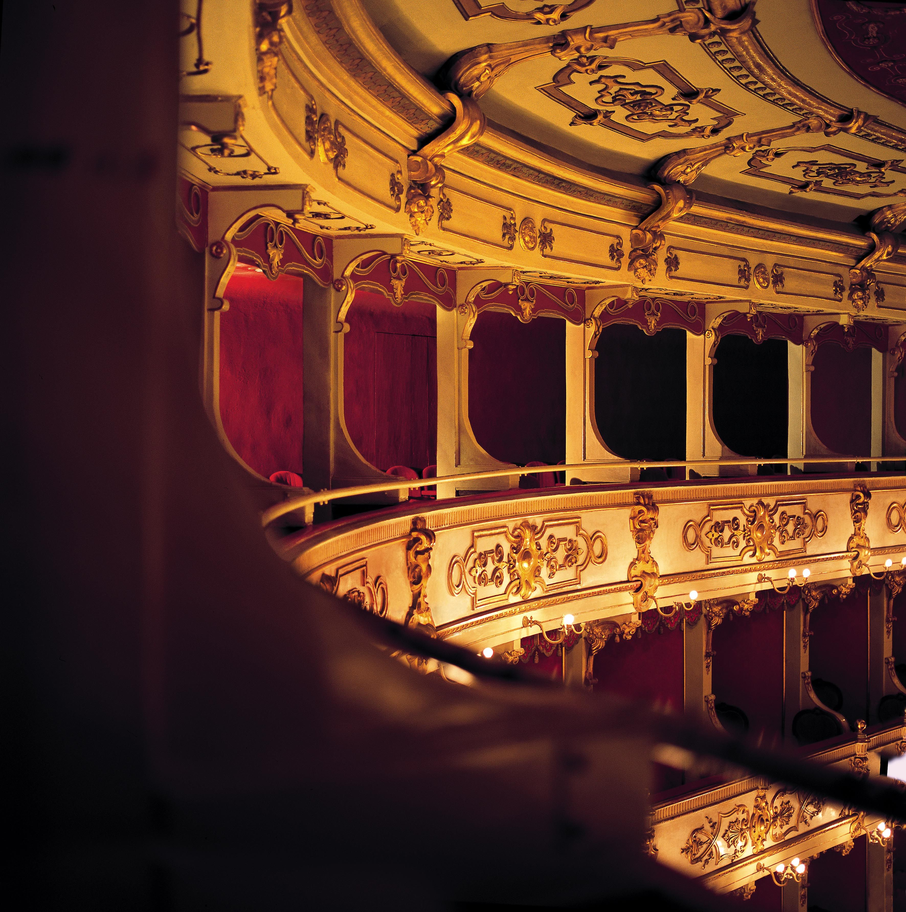 An ornate theater interior with a curved balcony and red curtains.