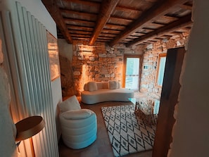 Ein gemütliches Zimmer mit einer Steinwand, einem weißen Sofa, einem runden Hocker und einem gemusterten Teppich.