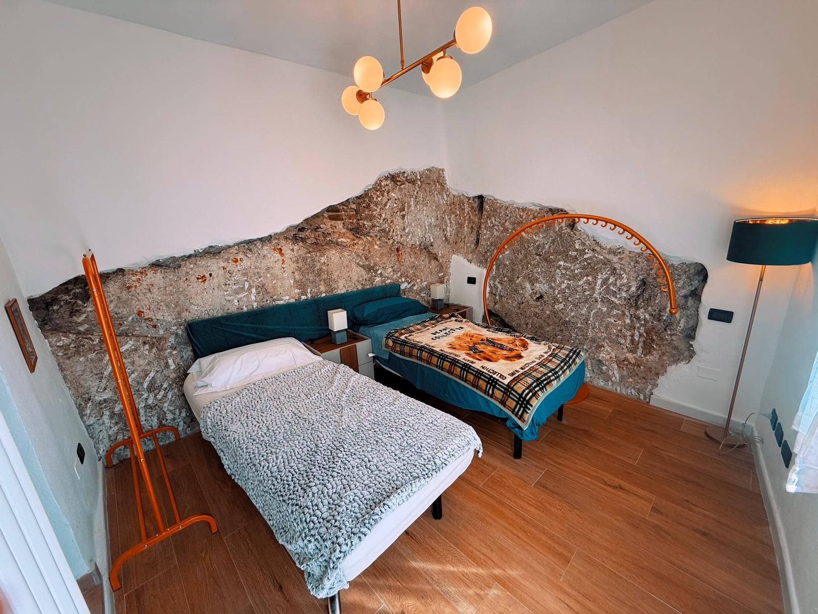 Una camera da letto con una parete in pietra rustica, due letti, una lampada da terra e un lampadario moderno.
