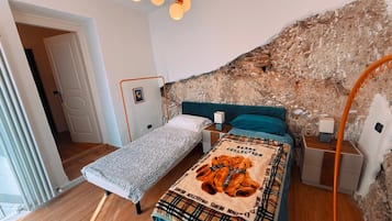Une chambre avec un plafond en pente, un lit recouvert d’une couverture à carreaux, une table de chevet et un mur en briques apparentes.