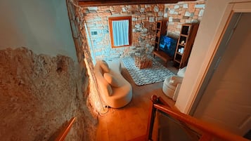 Une pièce aux murs de pierre, avec un canapé, un téléviseur et un escalier en bois.