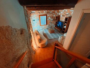 Ein Zimmer mit Steinwänden, einer Couch, einem Fernseher und einer Holztreppe.