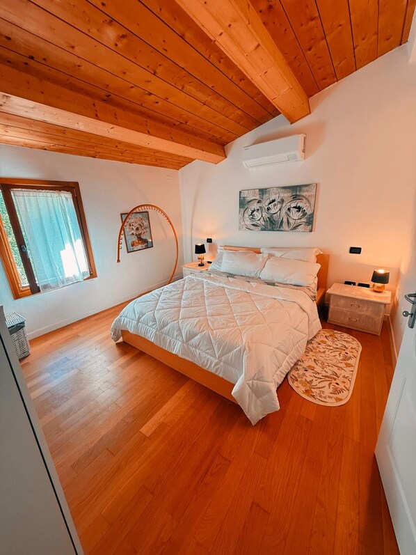 Ein Schlafzimmer mit Holzboden, einem Bett mit Patchworkdecke, einem Nachttisch mit Lampe und einem Fenster mit Vorhängen.