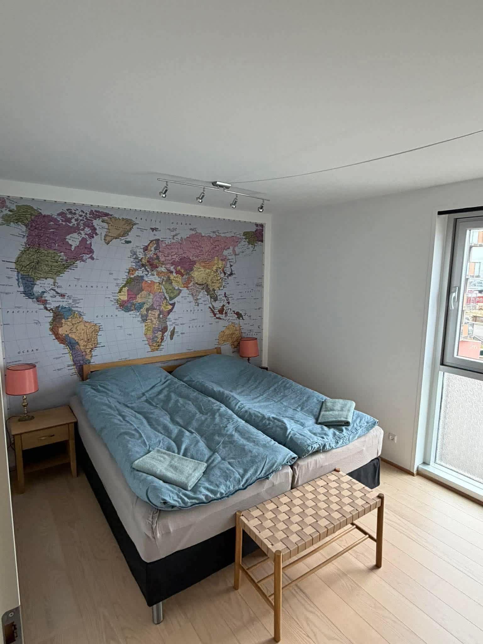 Une chambre à coucher avec un lit, un banc en bois, une table de chevet, une carte accrochée au mur et une fenêtre.