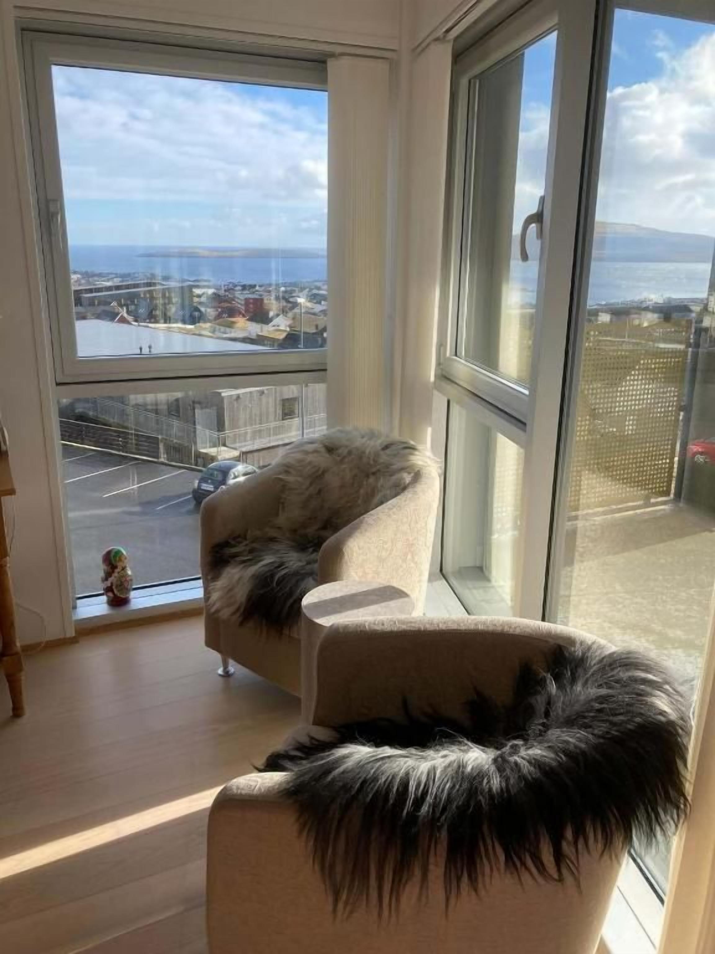A room with a large window, a sofa with a fur throw, and a view of a cityscape.