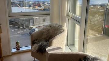 A room with a large window, a sofa with a fur throw, and a view of a cityscape.
