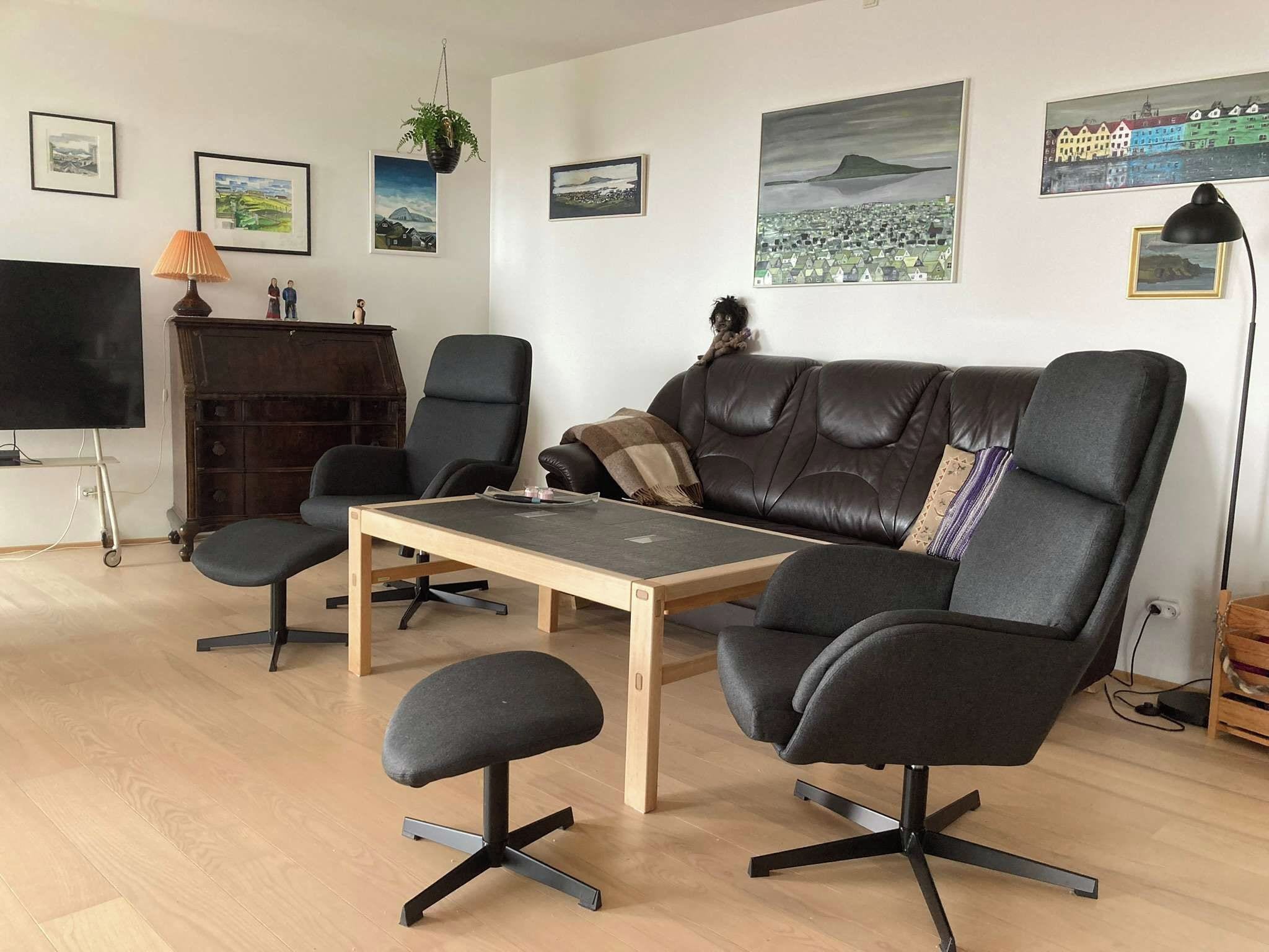 Una sala de estar moderna con un sofá de cuero, dos sillones, una mesa de centro y un televisor sobre un mueble.