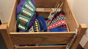 A wooden crate with a handle, containing various items including a purple knitted item, a multicolored knitted item, and a green package labeled 'SNELDAN'.