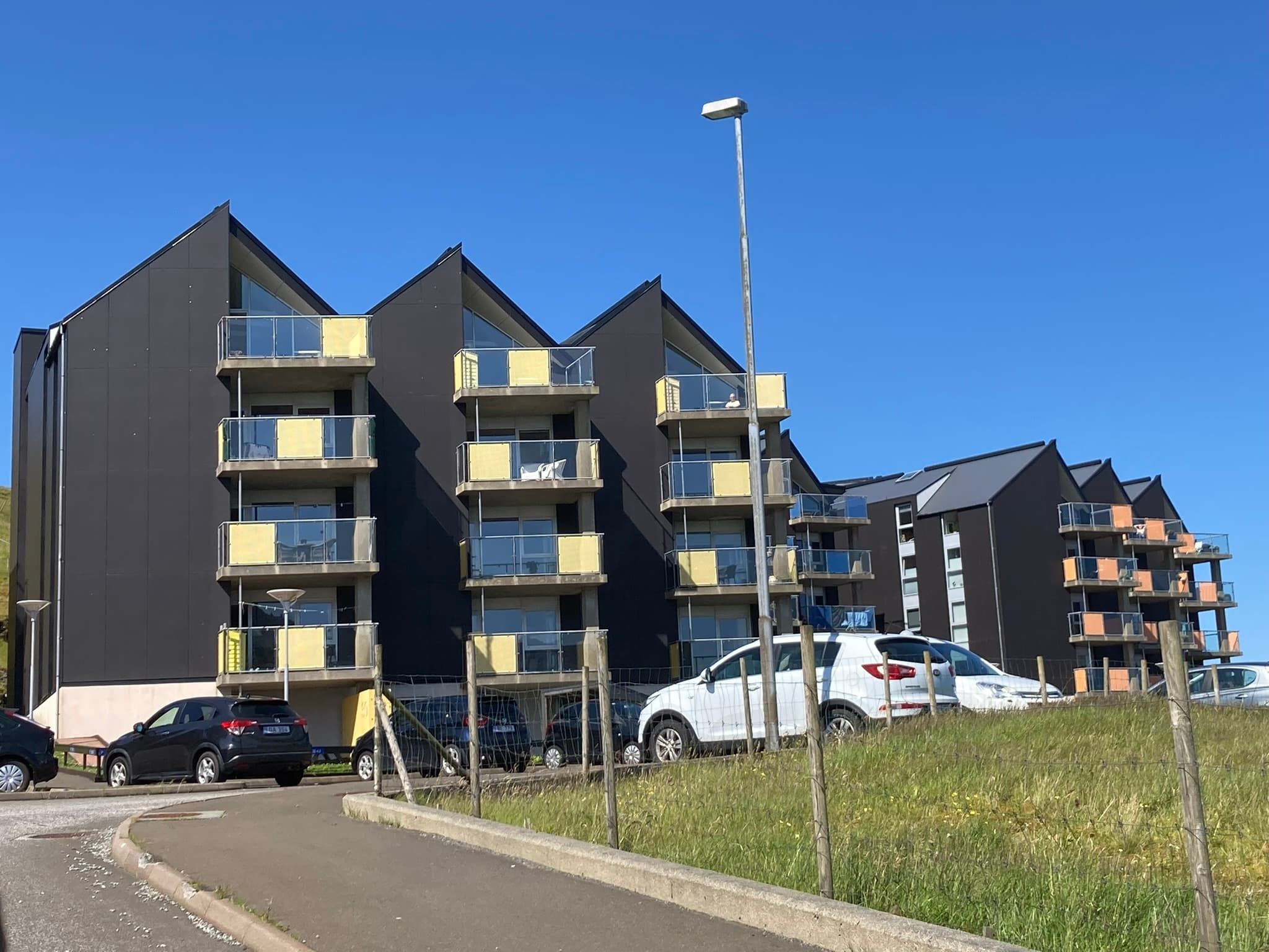 Een modern appartementencomplex met meerdere balkons en een parkeerplaats.