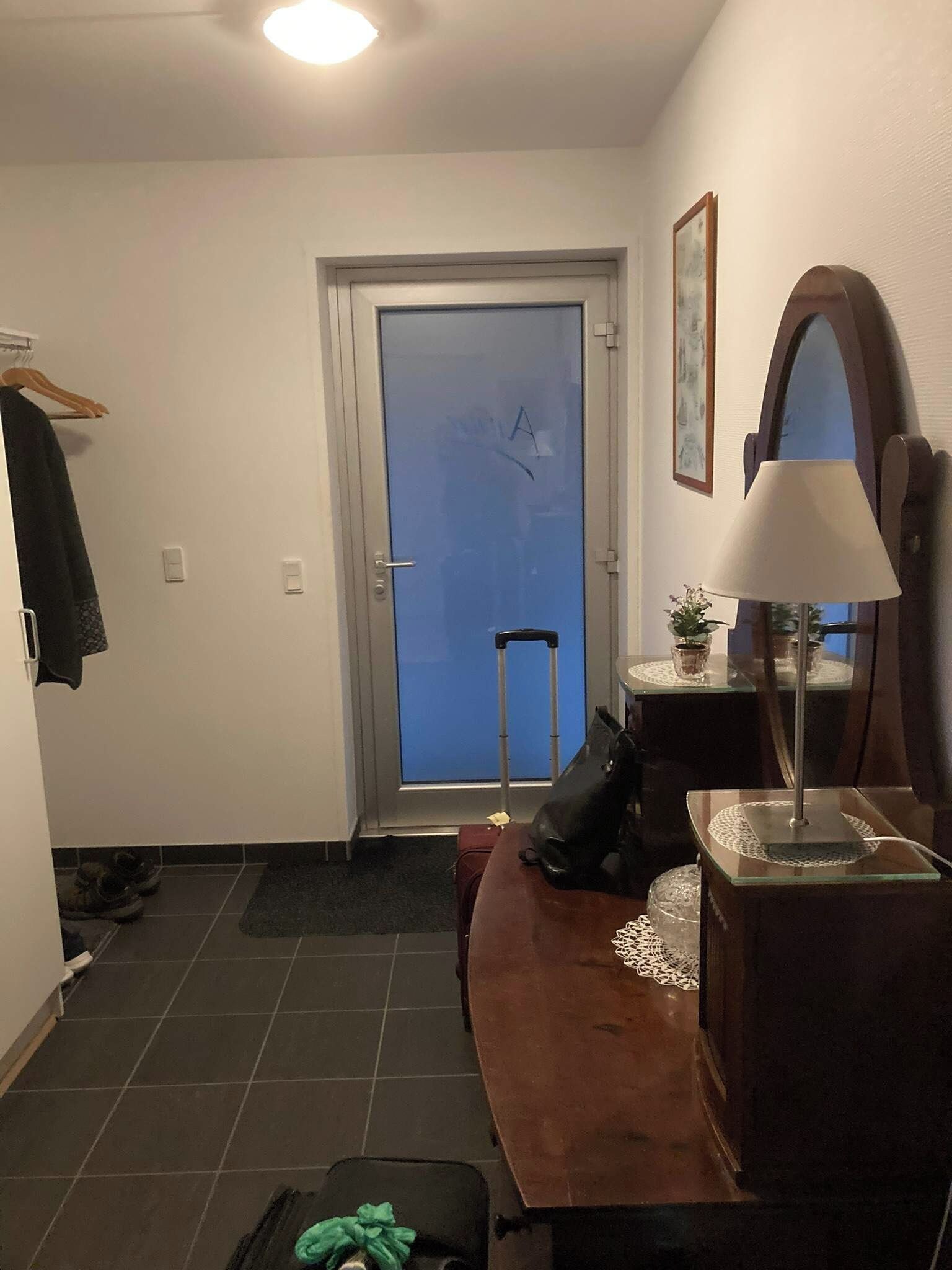 Una habitación de hotel con una puerta, una silla, un escritorio con lámpara y una maleta en el suelo.