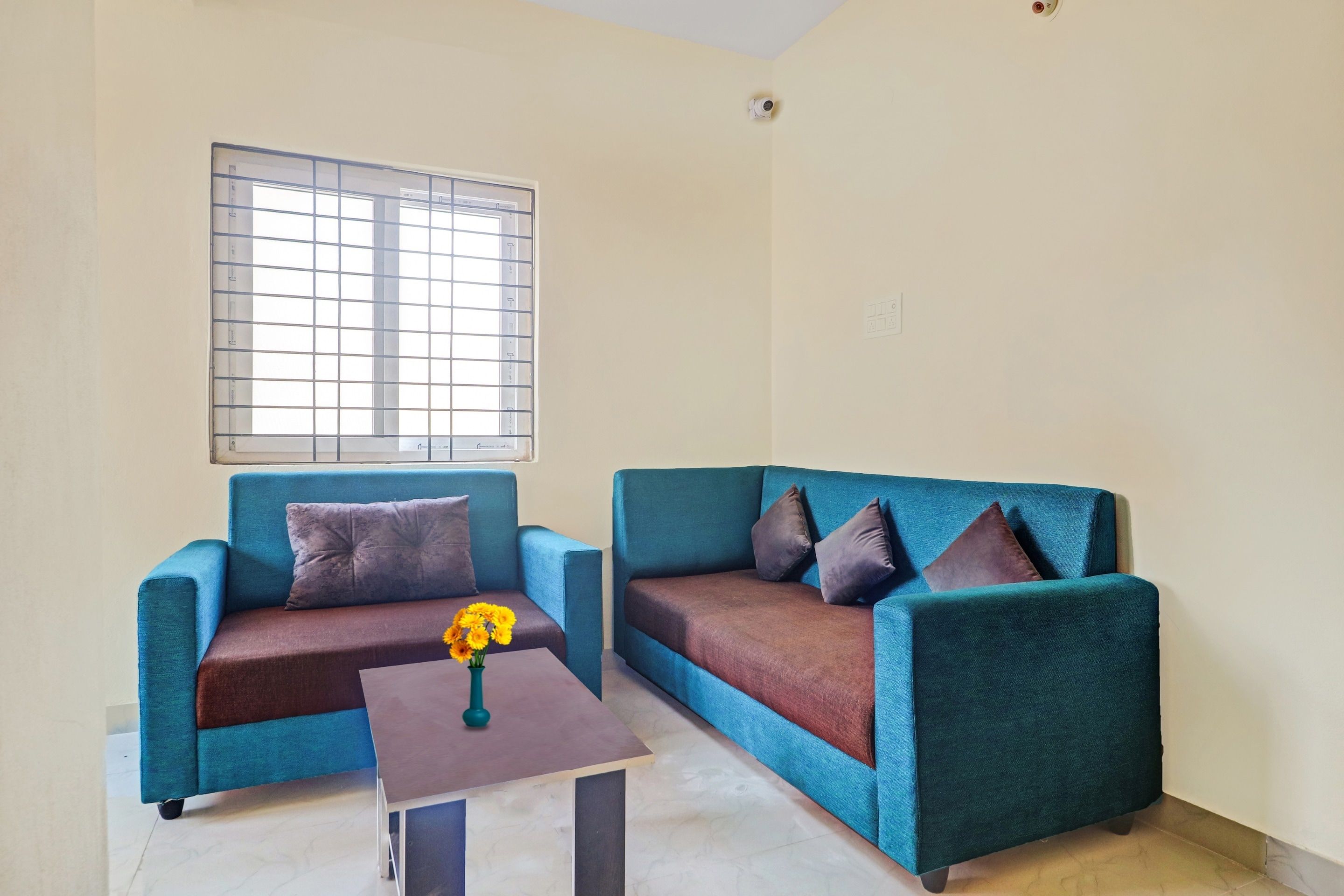 Una habitación con dos sofás azules, una mesita con un florero y una ventana con persianas.