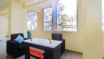 Una habitación con un escritorio negro con un logotipo rojo, dos sillas y un ventanal con vistas a árboles y edificios.