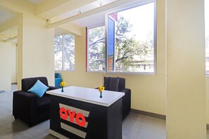 A room with a black desk featuring a red logo, two chairs, and a large window with a view of trees and buildings. - Collection O Elite Stay Near Habsiguda  (Hyderabad)