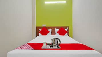 A hotel room with a bed, a bedside table with a kettle, and a red and white bedspread.