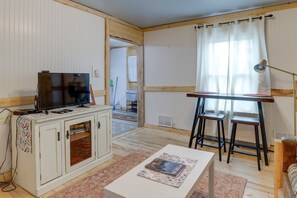 A room with a television on a cabinet, a table with magazines, a window with curtains, and a chair. - Lovely 2 bedroom apartment with patio and yard near downtown hospital (Casper)