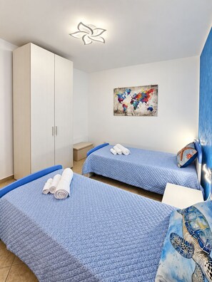 Ein Schlafzimmer mit zwei Betten, einem Kleiderschrank, einem Gemälde und einer dekorativen Deckenleuchte.