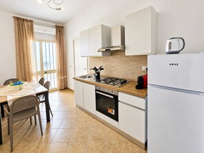 A compact kitchen with a gas stove, a built-in oven, a refrigerator, and a window with curtains. - Casa Brezza Private Garden Porto Cesareo (Porto Cesareo)