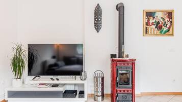 Una sala de estar con un televisor de pantalla plana, un horno de leña rojo, una planta en maceta y un cuadro en la pared.