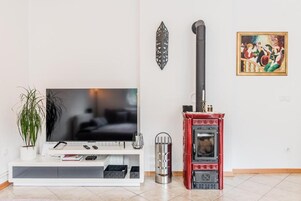 Una sala de estar con un televisor de pantalla plana, un horno de leña rojo, una planta en maceta y un cuadro en la pared.