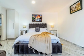 Une chambre à coucher moderne avec un grand lit, deux lampes de chevet, un tableau au mur et un sol en marbre.