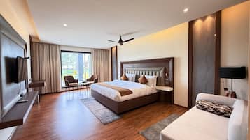 A modern hotel room with a large bed, a seating area with chairs, a flat-screen TV mounted on the wall, and a ceiling fan.