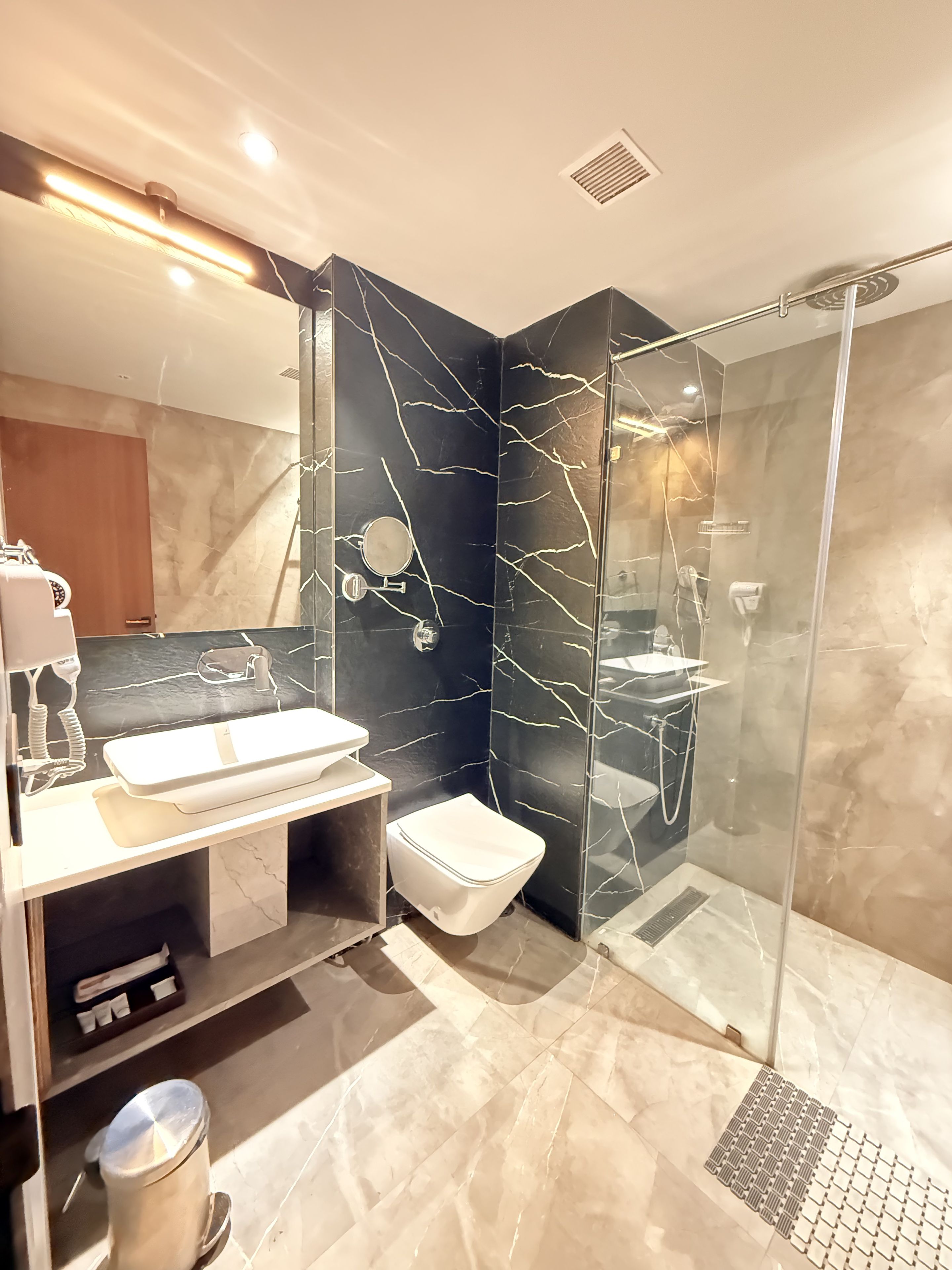 A modern bathroom with a glass-enclosed shower, a white sink, and a marble-tiled floor.
