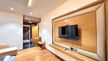 A modern living room with a flat-screen TV mounted on a wooden wall, a wooden floor, and a seating area with a sofa and a coffee table.