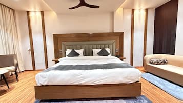 A modern hotel room with a wooden bed, a sofa, a desk, and a ceiling fan.